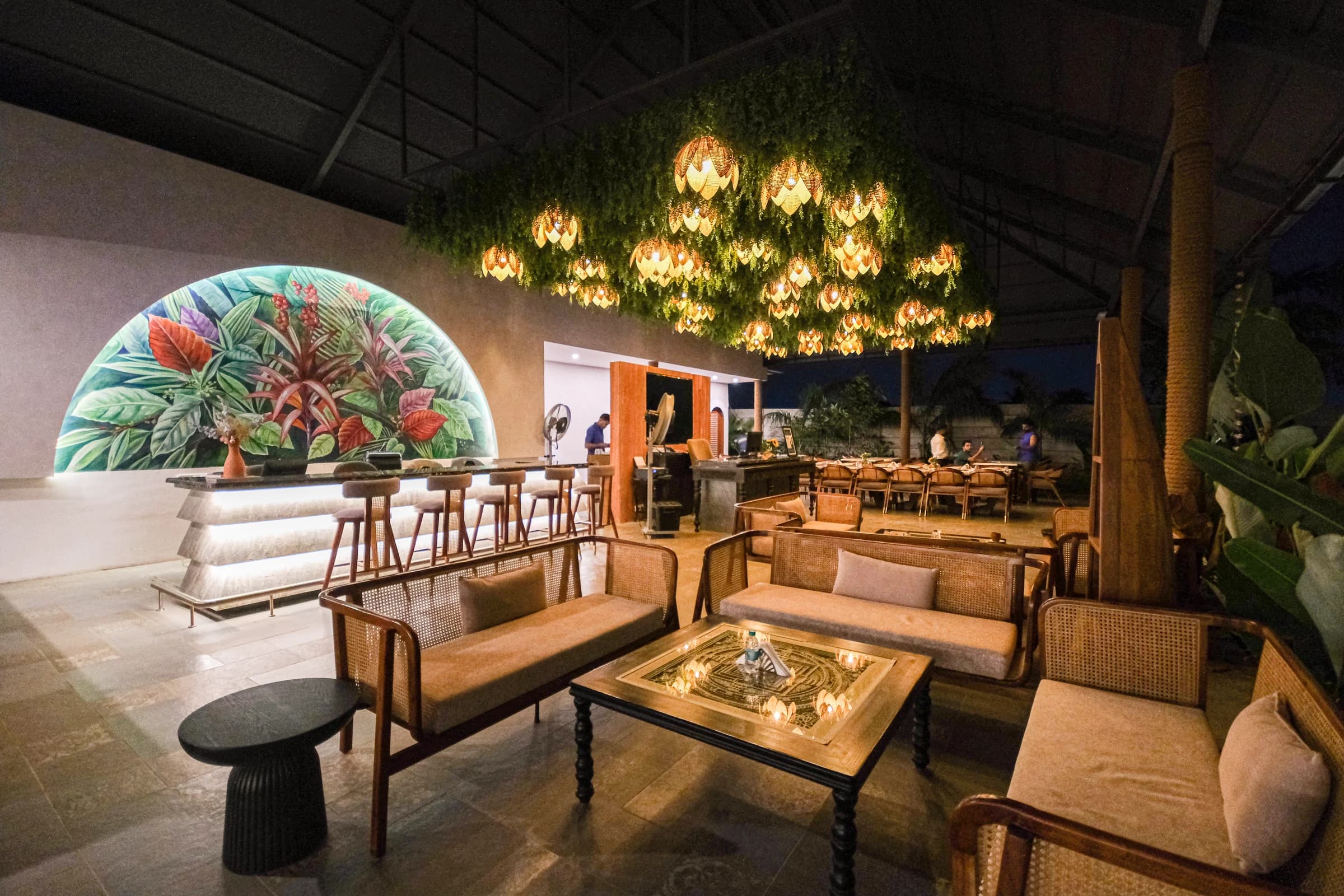 Samsara reception lounge at night, with woven sofas, a botanical mural and glowing pendant lamps
