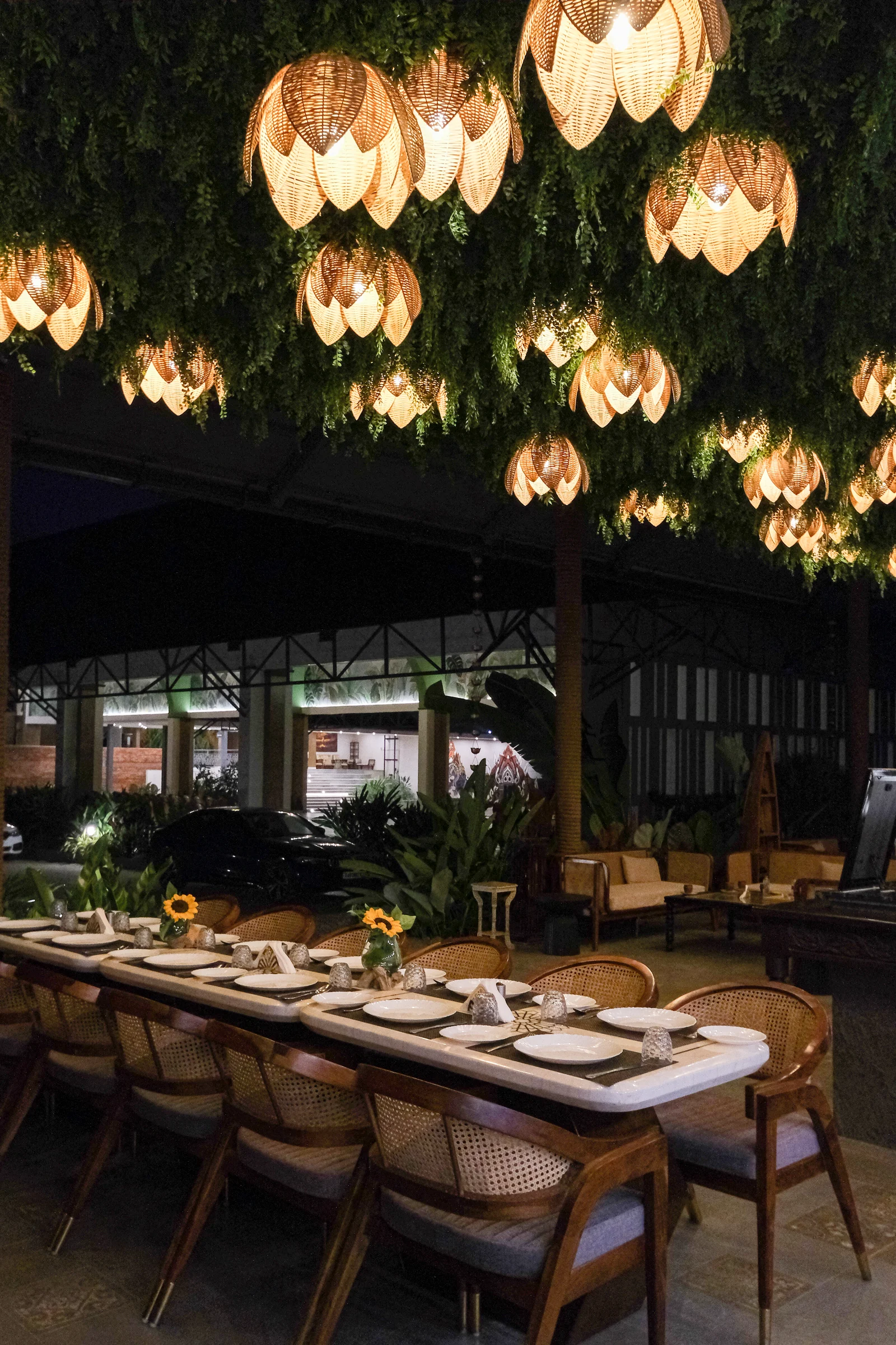 Glowing woven lamps and a leafy ceiling above Samsara’s restaurant dining table at night