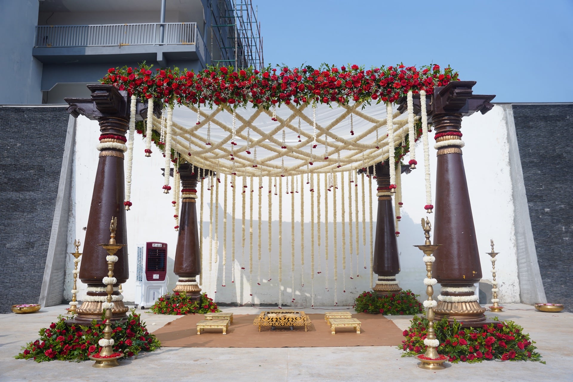 A traditional South Indian mandap with carved pillars and red roses
